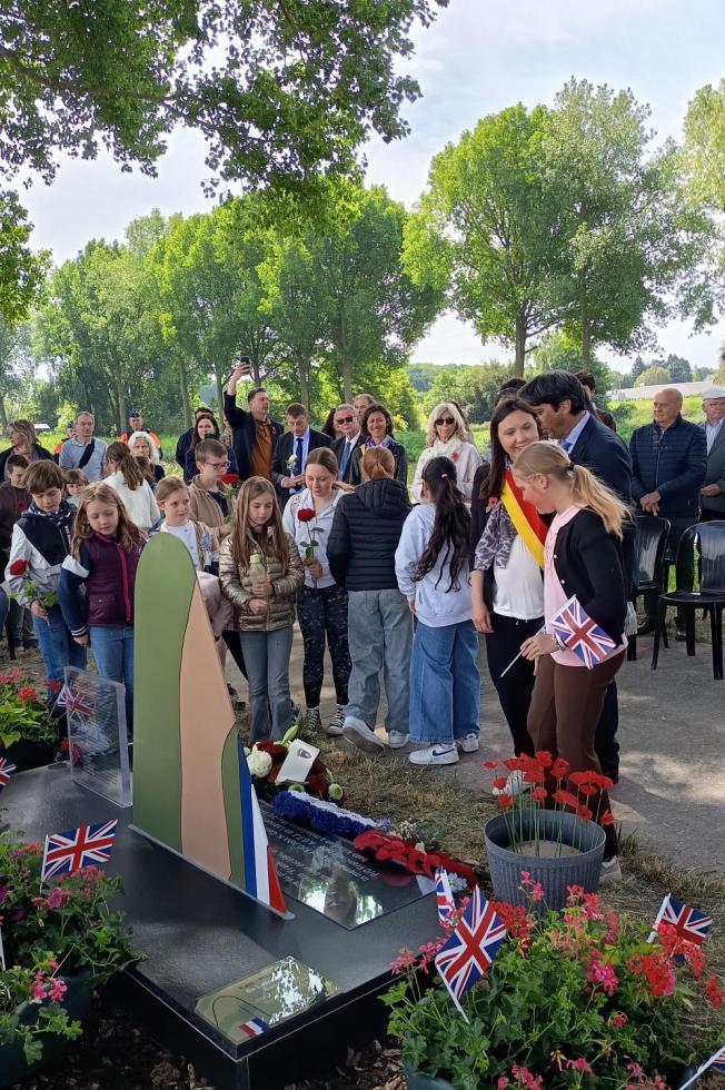 Des enfants et des élus participent à une cérémonie commémorative autour d’un mémorial fleuri