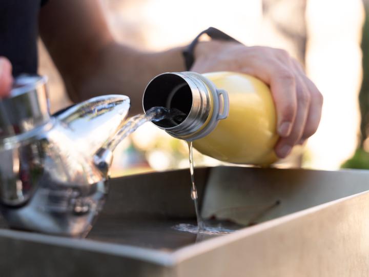 Une personne remplit une gourde jaune avec de l'eau d'une fontaine publique.